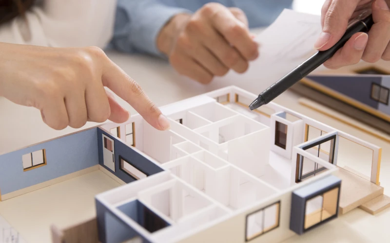 H&auml;nde zeigen auf ein aufgeschnittenes wei&szlig;es Architekturmodell eines Hauses
