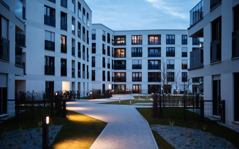 Moderne Wohnanlage mit hellen Mehrfamilienh&auml;usern und beleuchtetem Innenhof am Abend