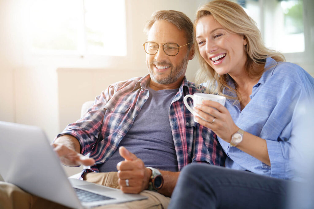 Paar mit Kaffeetasse sitzt lachend vor einem Laptop